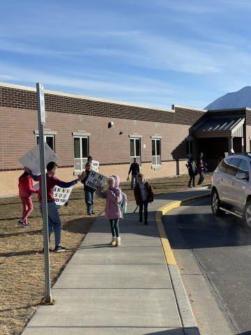 Students in front of school encouraging parents to honk for kindness and welcoming the students to school.