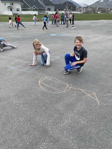 Students drawing shapes on the playground with chalk.