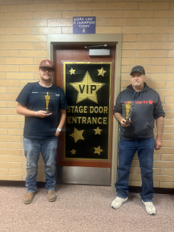 Mr. Daybell and Mr. Ferran holding trophies in front of their office door.