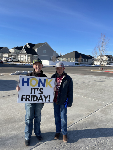 Students in front of school encouraging parents to honk for kindness and welcoming the students to school.