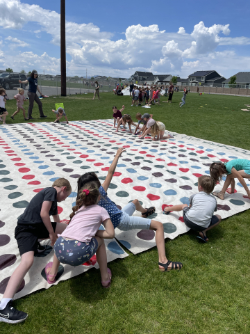 Students playing a game of Twister on a giant playing board on the field.