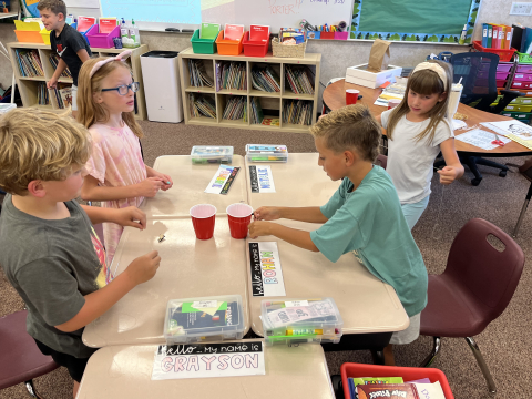 Students picking up a cup of marbles using creative strategies to get them all in an