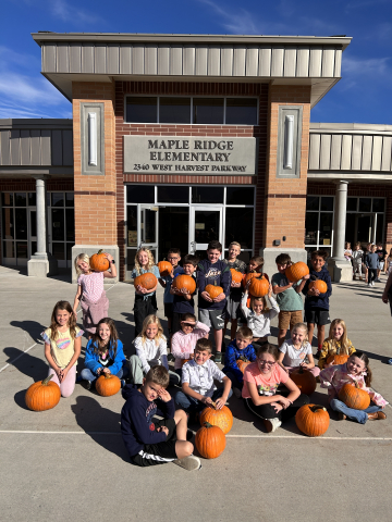 Students holding their pumpkins in front of Maple Ridge.