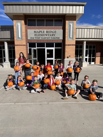Students holding their pumpkins in front of Maple Ridge.
