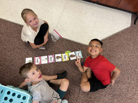 Kids sitting on the floor with cards that have sequence words on them.